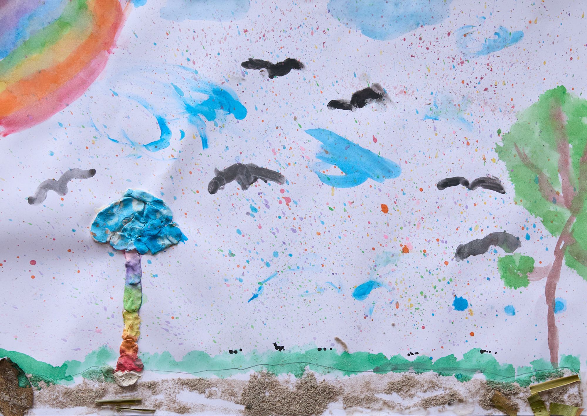 Child's painting of a colorful rainbow in the top left corner, a blue tree with a rainbow trunk, a green tree, black birds in the sky, and a grassy field.